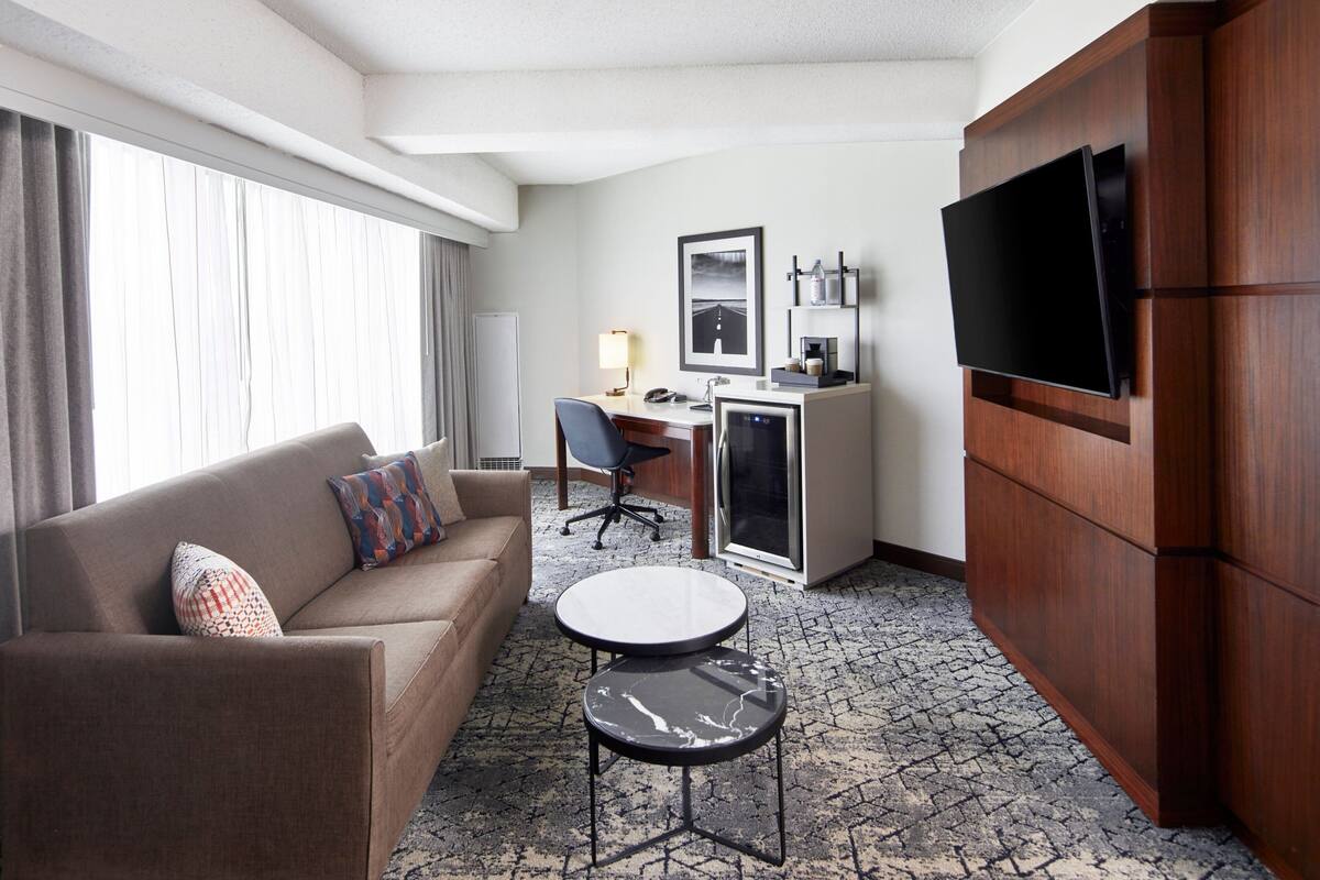 Et hotelværelse med sofa, skrivebord, fjernsyn og minibar.