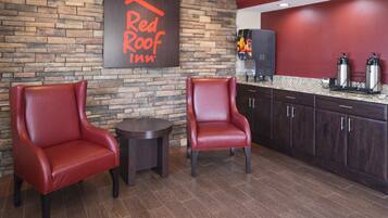 Lobby do Red Roof Inn com duas poltronas de couro, uma mesa redonda pequena e uma área de cozinha com máquina de café e duas garrafas térmicas.