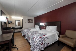 Habitación de hotel con dos camas, un escritorio, una silla y un televisor.