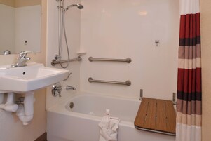 Un baño con lavamanos blanco, bañera y ducha. Se instalaron barras de apoyo para mayor seguridad.