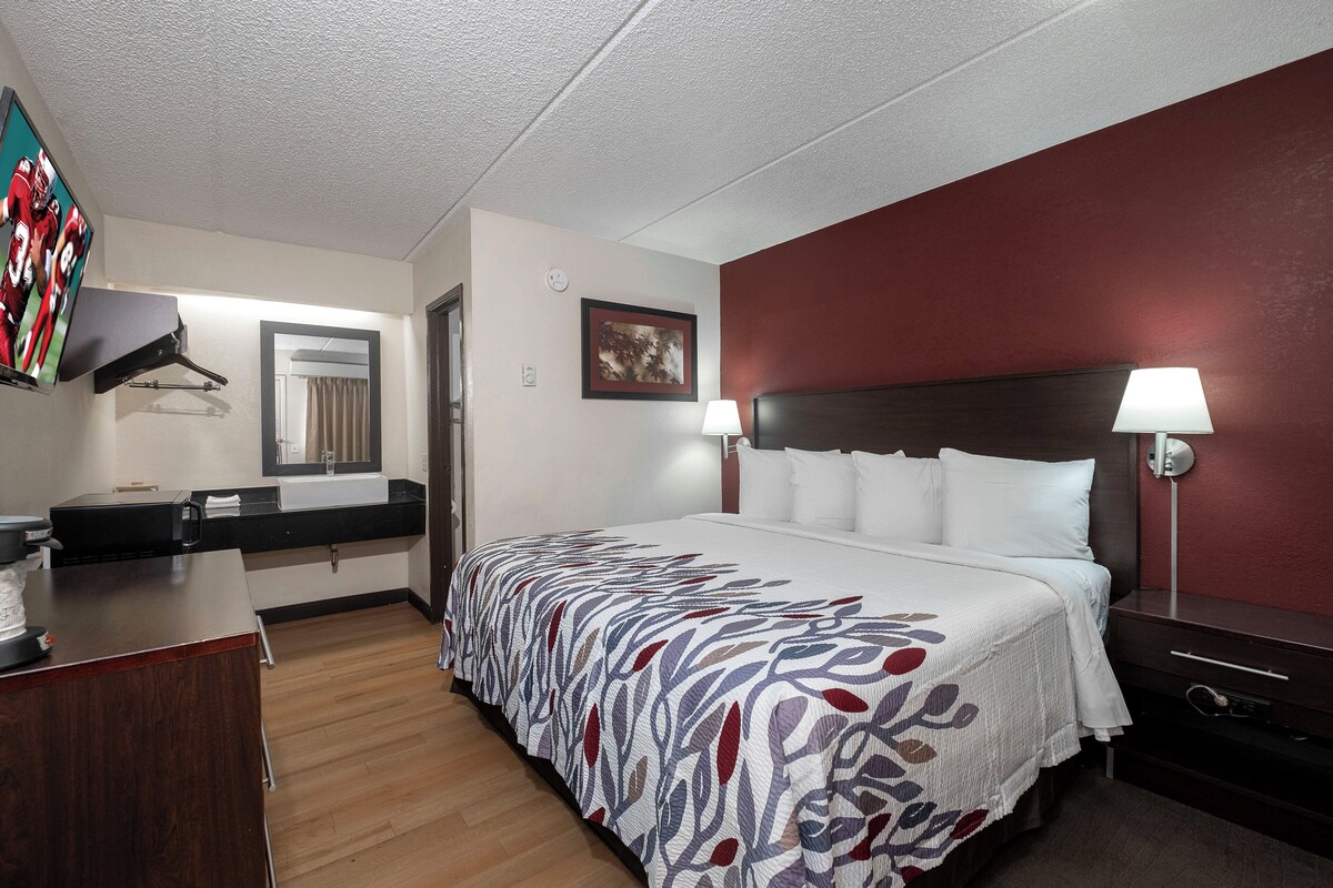 A hotel room with a bed, bedside lamps, a desk, a mirror, and a wall-mounted TV.