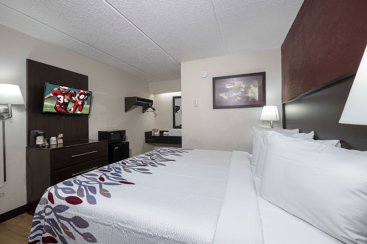 A hotel room with a large bed, a flat-screen TV mounted on the wall, a desk with a lamp, and a small table with a coffee maker.
