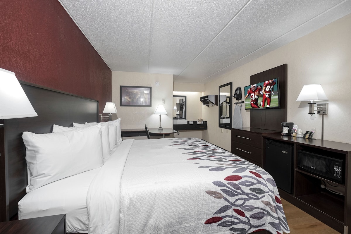 A hotel room with a large bed, a desk, a chair, a TV, a microwave, and a coffee maker.