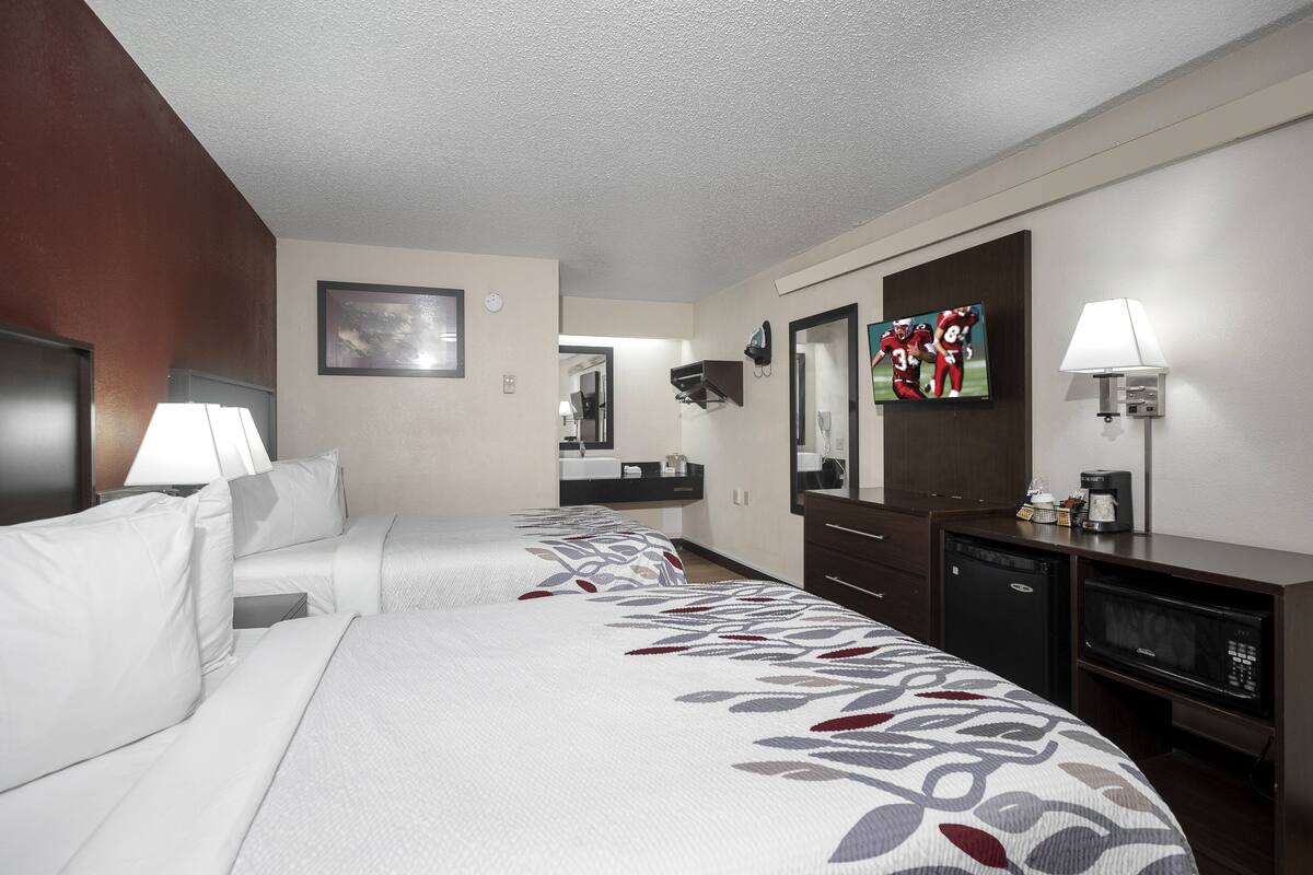 A hotel room with two beds, a desk with a computer, a microwave, and a TV.