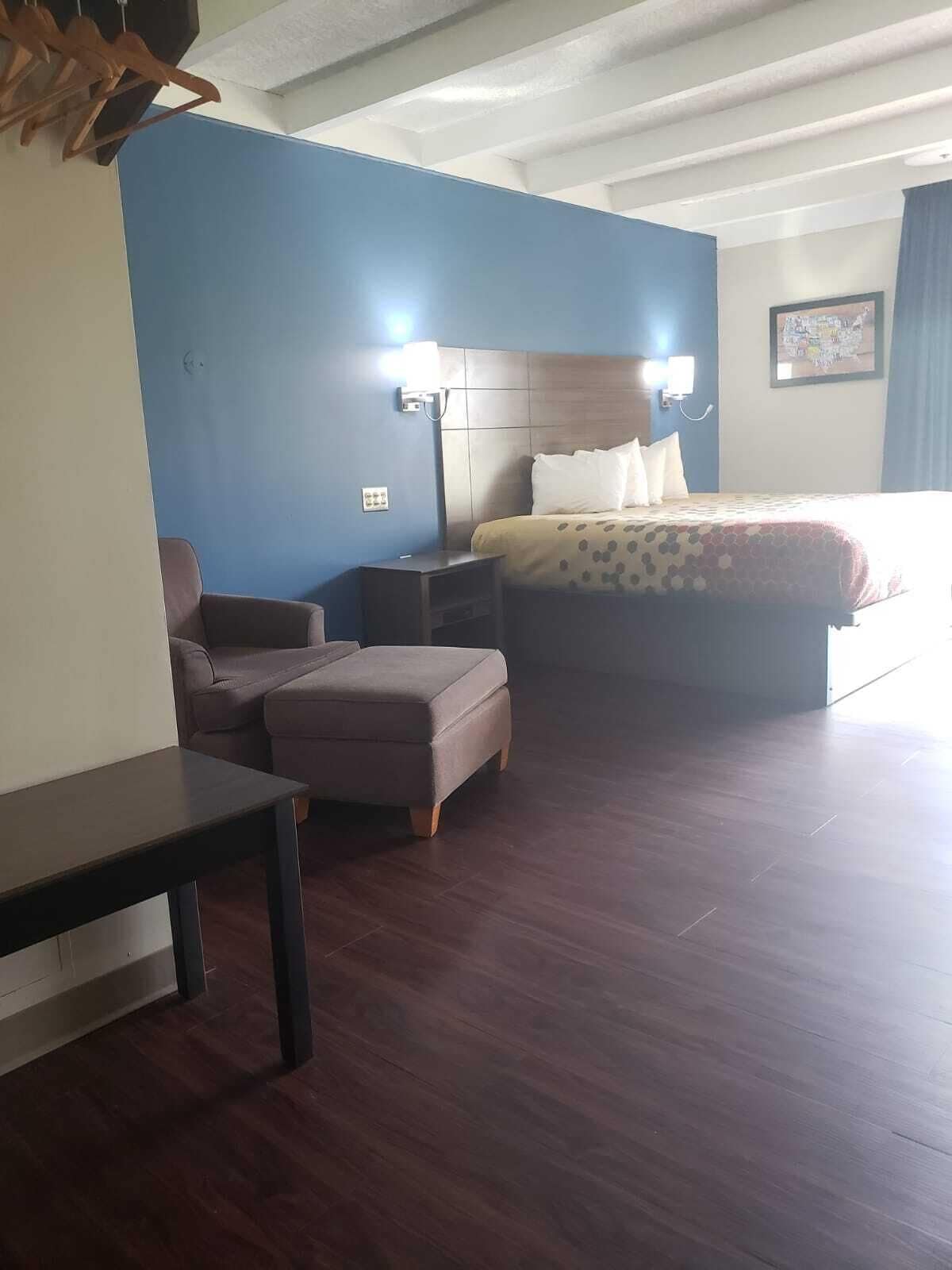 A hotel room with a bed, a nightstand, a chair, and a small table.