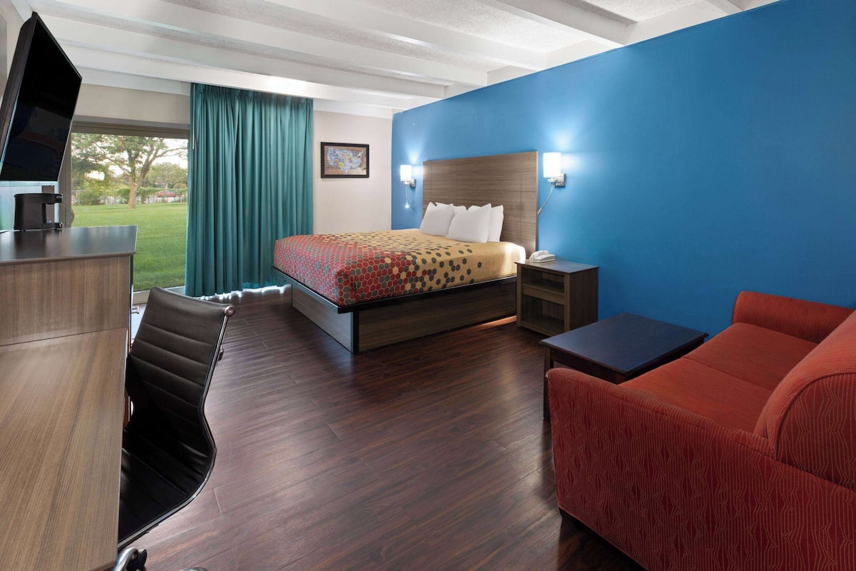 A hotel room with a bed, a desk, a chair, a sofa, and a TV.