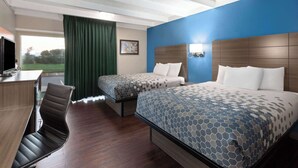Habitación de hotel con dos camas, un escritorio, una silla y un amplio ventanal con vistas a un paisaje verde.