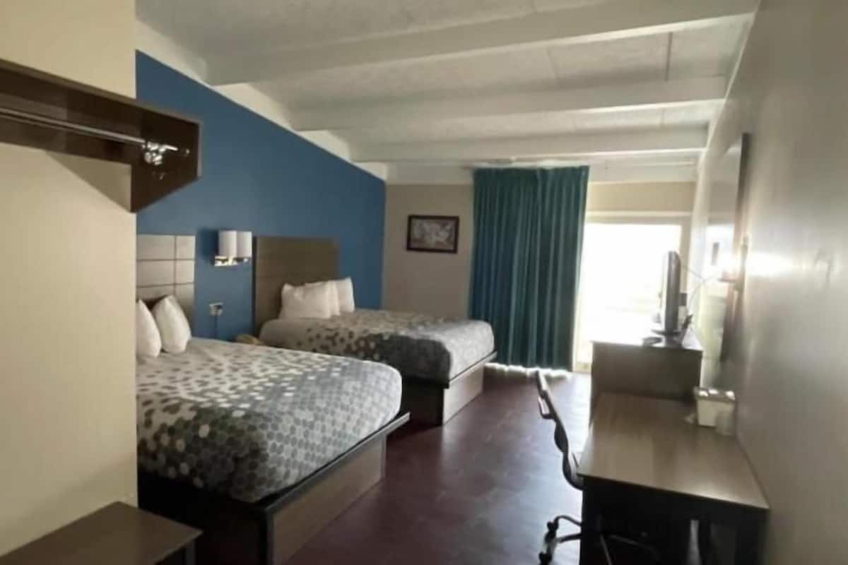 A hotel room with two beds, a desk, a chair, a TV, and a window with curtains.