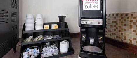 A coffee machine with a sign that reads "YOUR morning coffee" and a shelf with disposable cups and coffee pods.