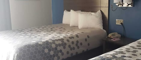 Habitación de hotel con dos camas, cabecero de madera, teléfono en la pared y un cuadro enmarcado.
