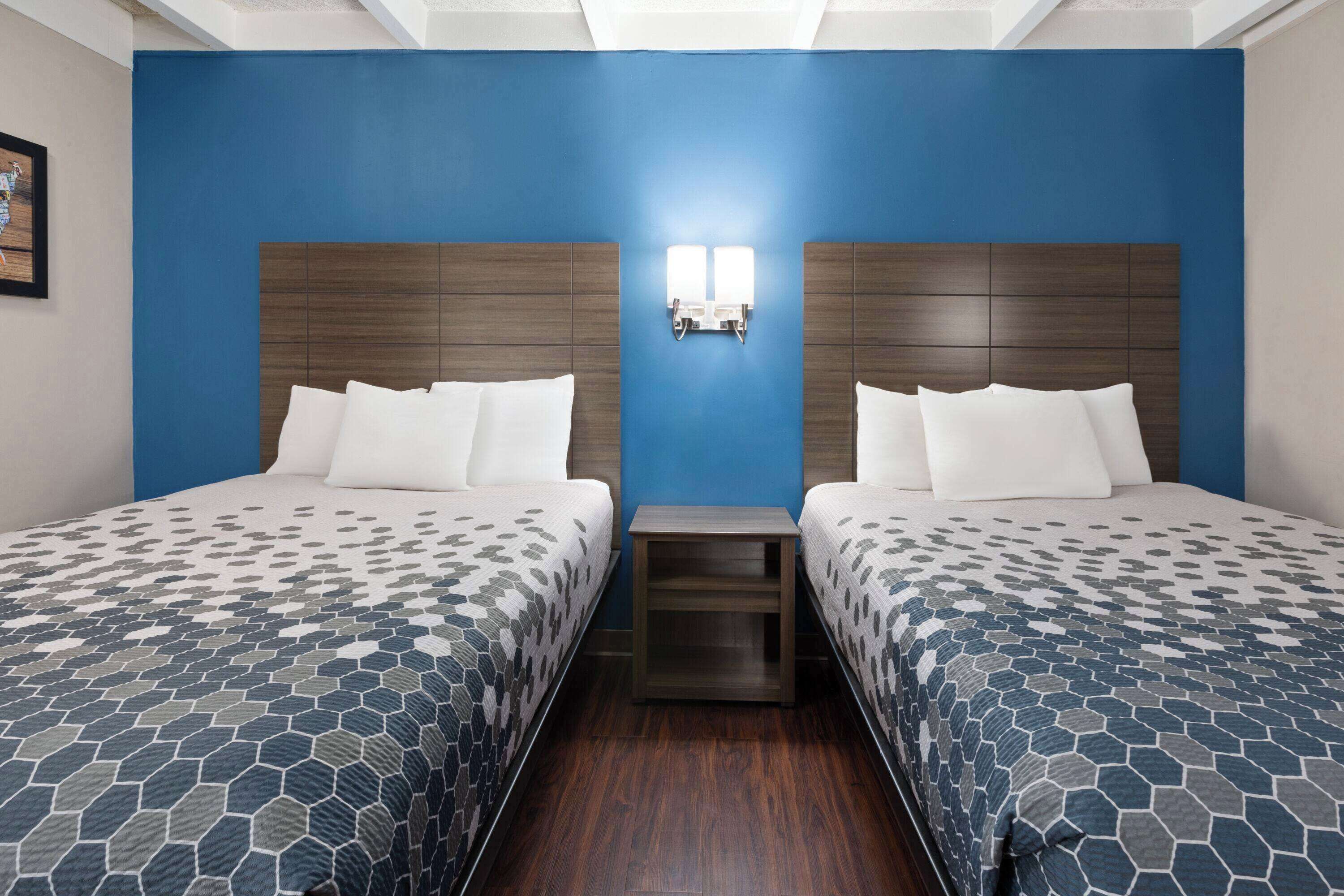 A hotel room with two beds, a blue accent wall, and a wooden headboard.