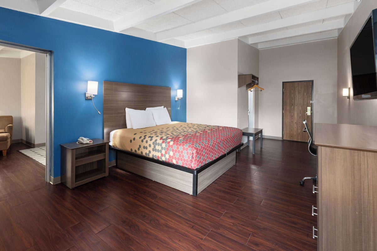 A modern hotel room with a large bed, a desk, a chair, a wardrobe, and a television.