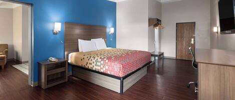 A modern hotel room with a large bed, a desk, a chair, a wardrobe, and a television.