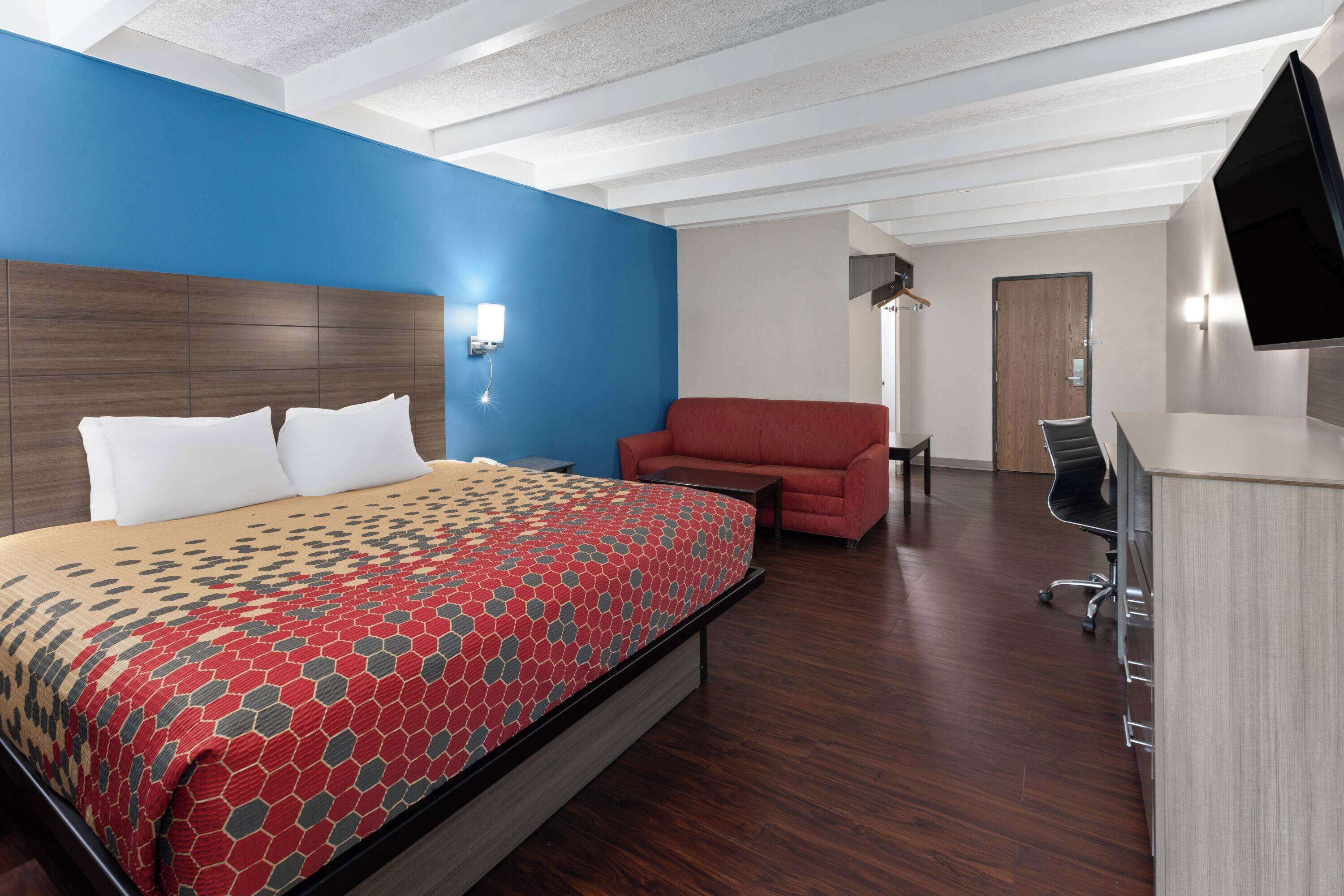 Habitación de hotel con una cama grande, un sillón rojo, un escritorio y un televisor montado en la pared.
