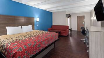 Habitación de hotel con una cama grande, un sillón rojo, un escritorio y un televisor montado en la pared.
