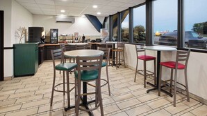 Un interior de restaurante con varias mesas y sillas, una zona de cocina y grandes ventanales que ofrecen vistas al exterior.
