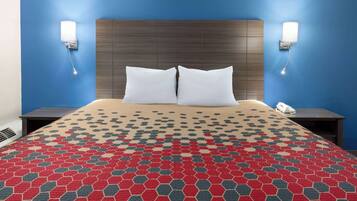 A hotel room with a large bed, two white pillows, a patterned red and gray bedspread, a wooden headboard, and two bedside lamps.