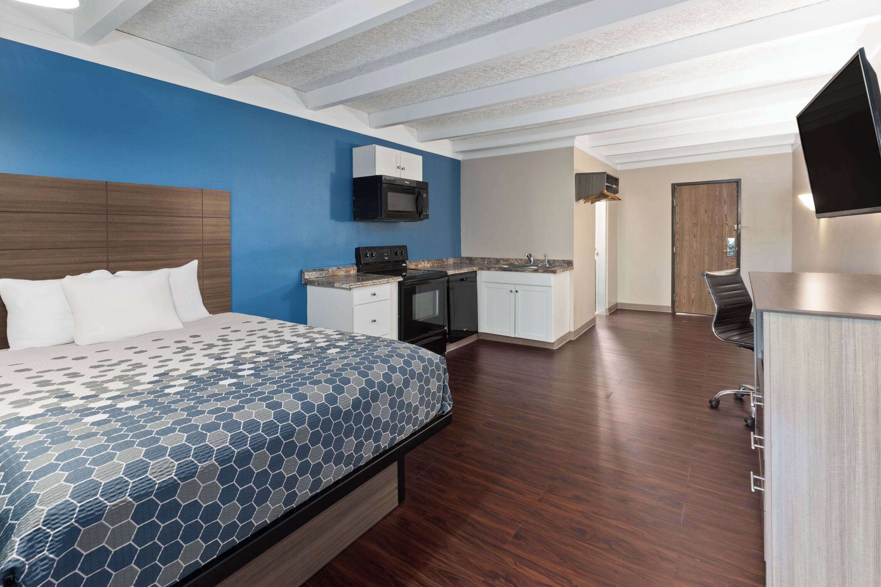 Una habitación de hotel moderna con una cama grande, una kitchenette, un televisor de pantalla plana y piso de madera.