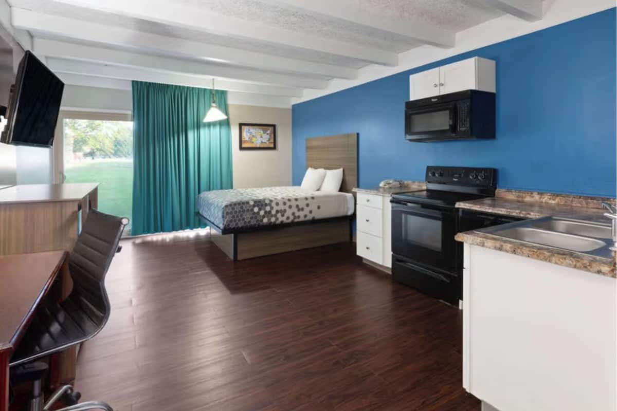 A compact room with a bed, kitchenette, and a TV.