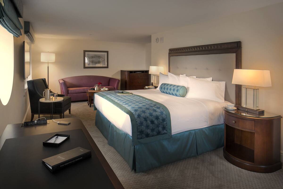 A hotel room with a bed, a desk, a chair, a sofa, and a nightstand with lamps.