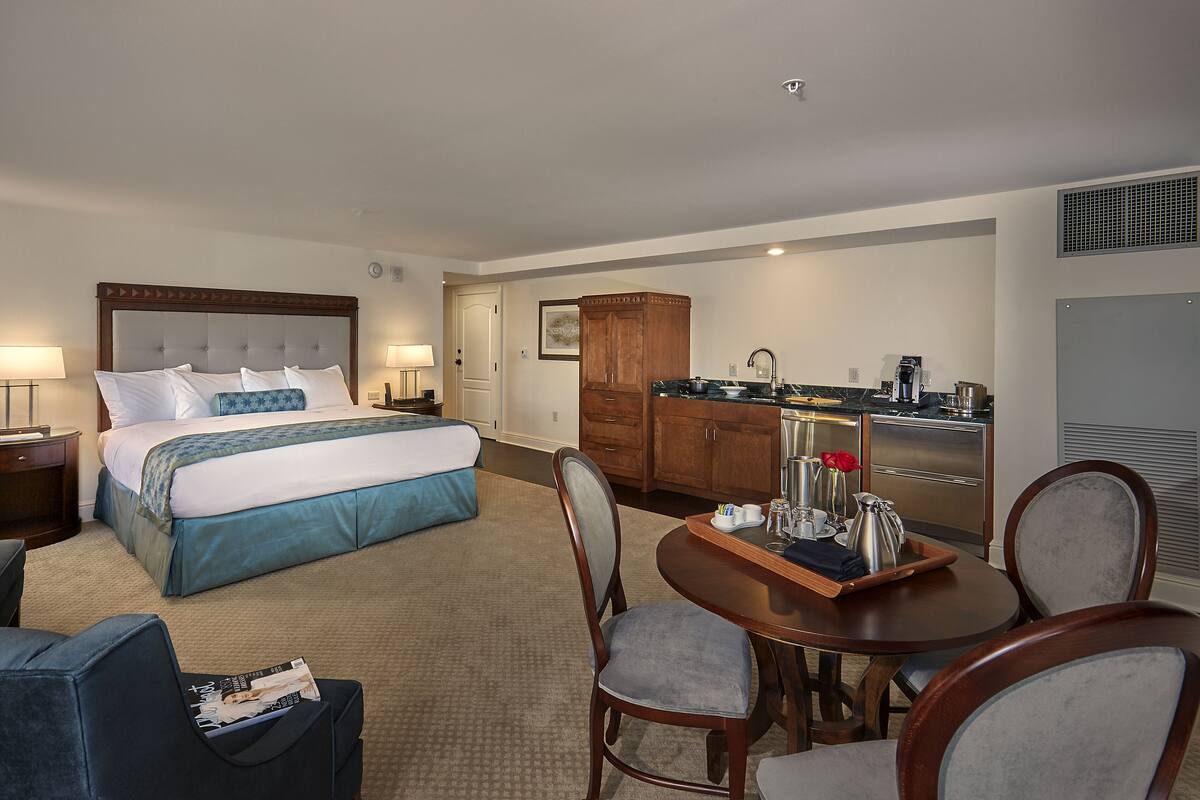 A hotel room with a bed, a dining table with chairs, a kitchen area, and a bathroom.
