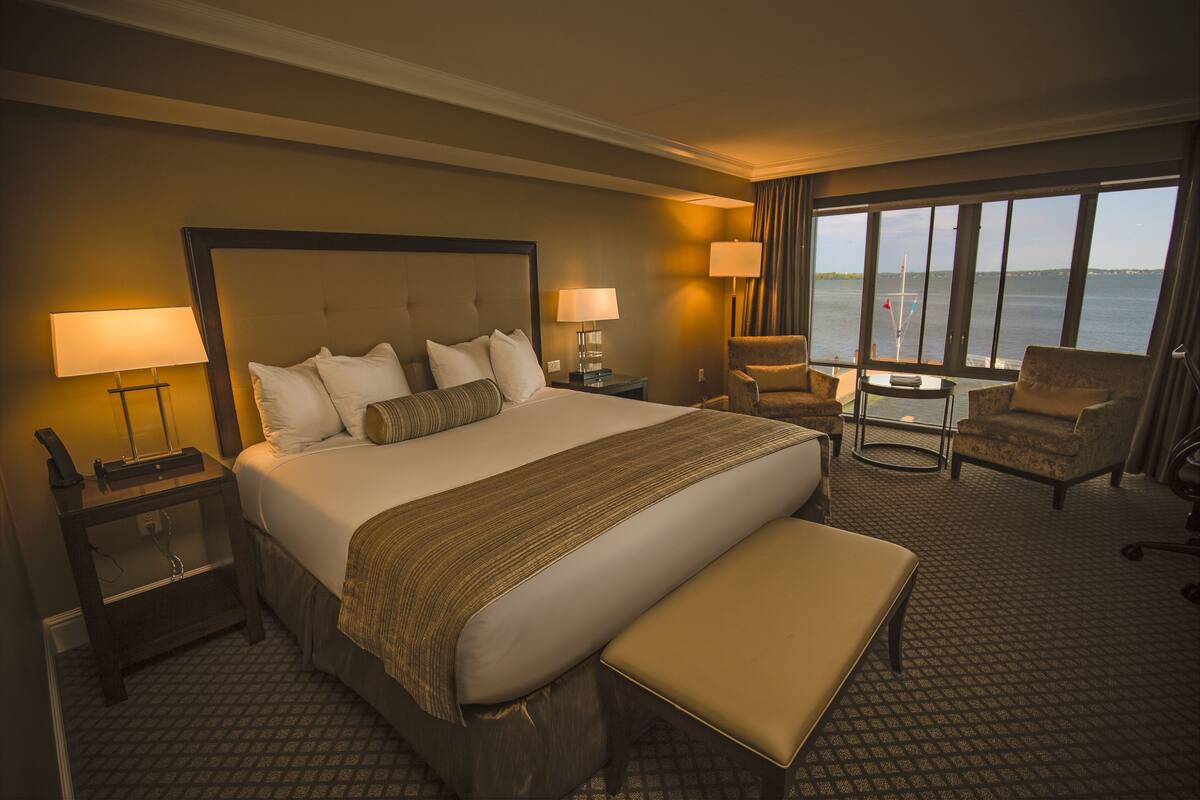 A hotel room with a large bed, two bedside tables, a chair, a small table, and a view of the water.