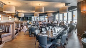 A spacious restaurant with high ceilings, pendant lighting, and large windows offering views of the city.