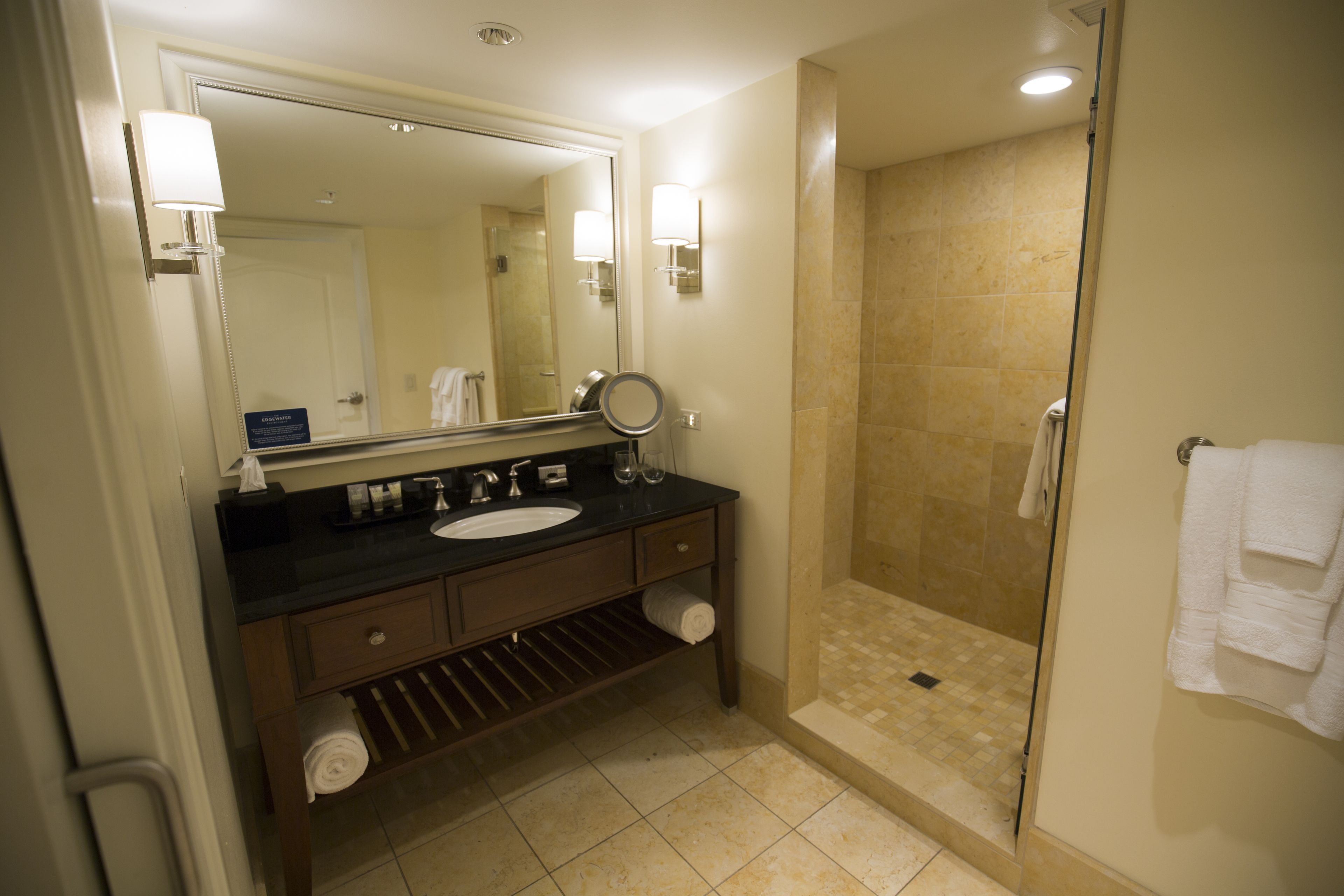 A hotel bathroom with a large mirror, a sink, a shower, and a towel rack.