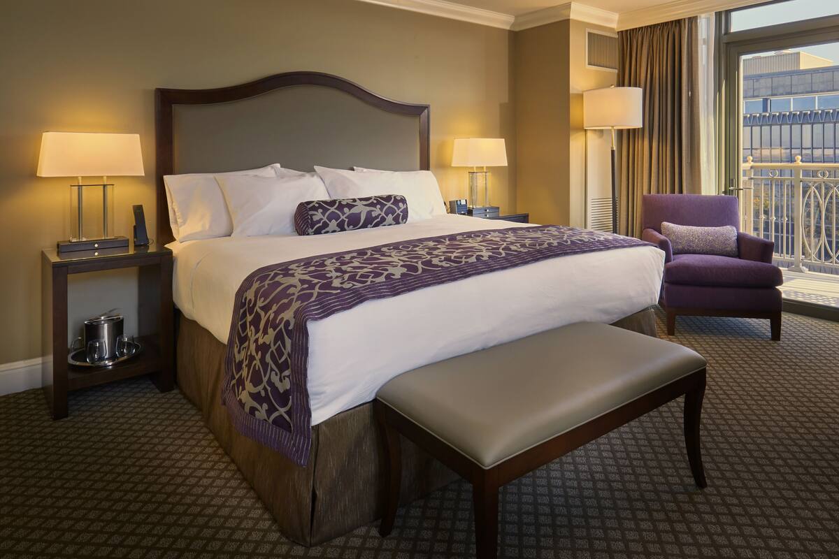 A hotel room with a large bed, two bedside tables with lamps, a chair, and a balcony view.