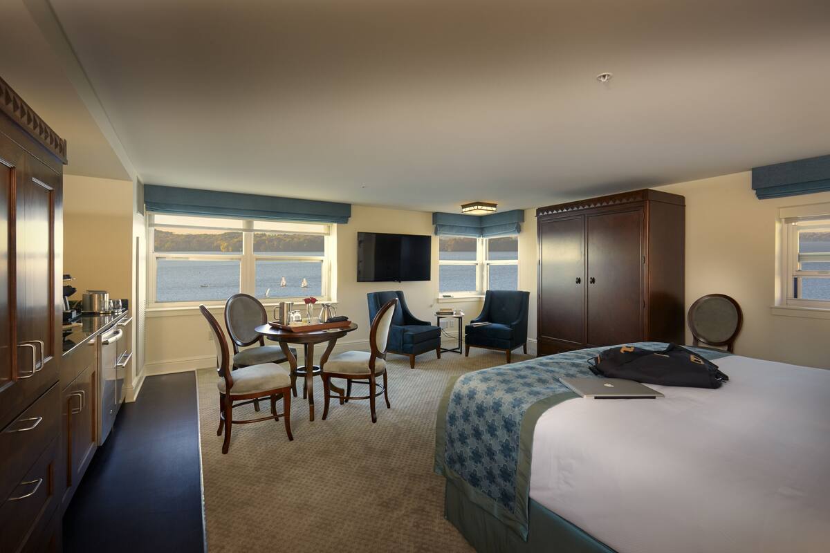 A hotel room with a bed, a desk with a chair, a TV, and a view of the sea.