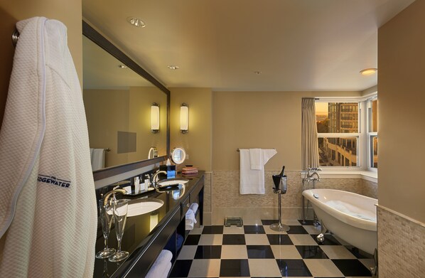 A hotel bathroom with a checkered floor, a large mirror, two sinks, a bathtub, and a window with a view of buildings.