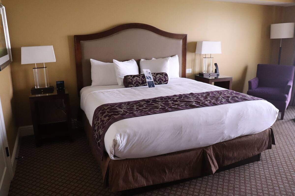 A hotel room with a large bed, two bedside tables, a chair, and a lamp on each side of the bed.