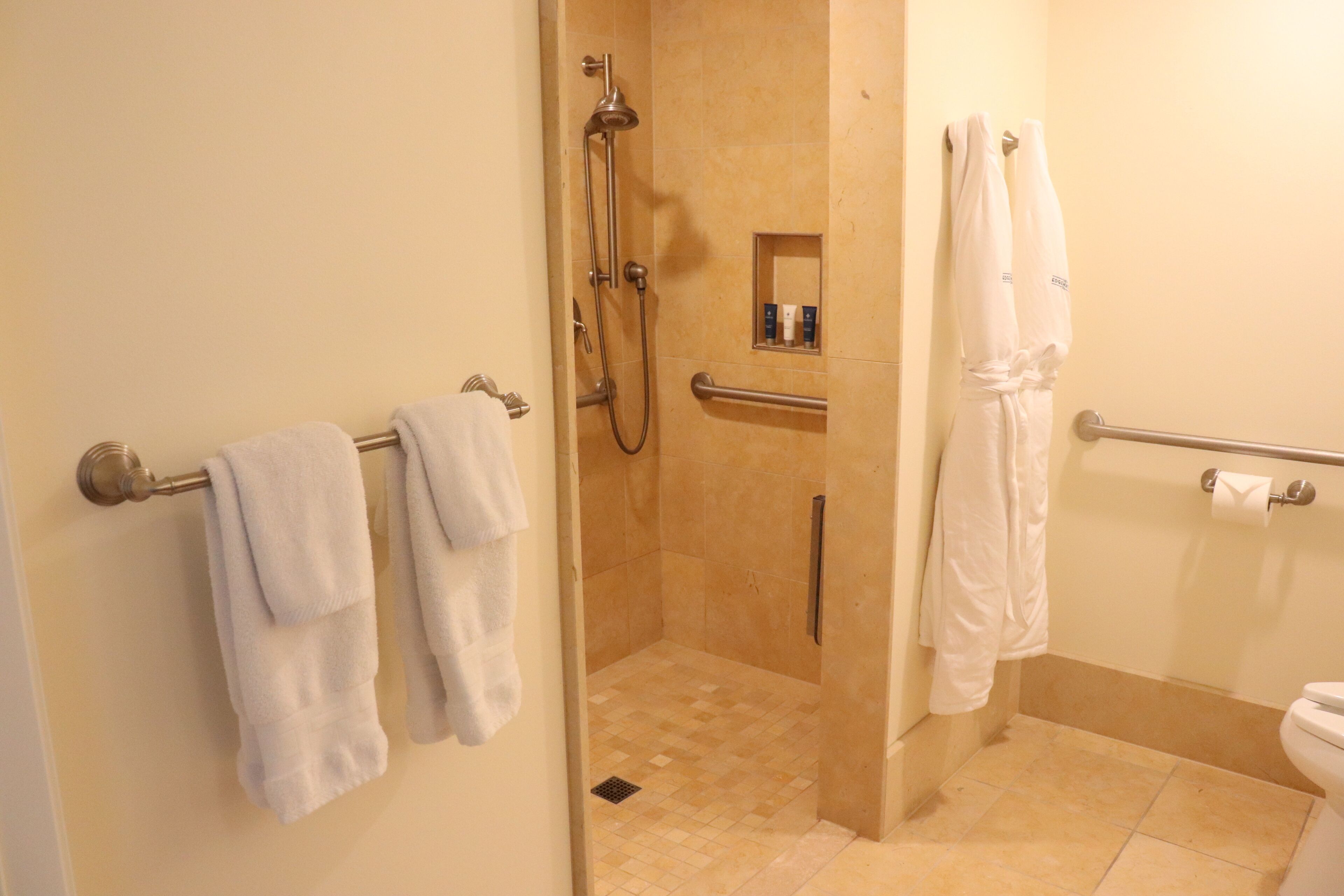 A bathroom with a shower, a toilet, and a towel rack with towels.