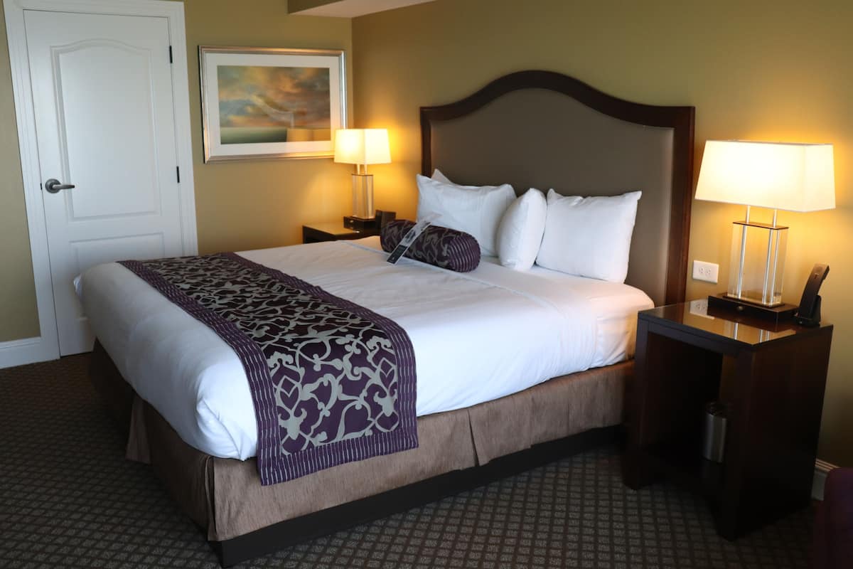 A hotel room with a large bed, two bedside tables with lamps, a door, and a framed picture on the wall.