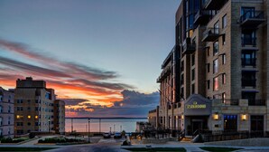 A hotel with a view of the water at sunset, featuring a prominent entrance and multiple balconies.