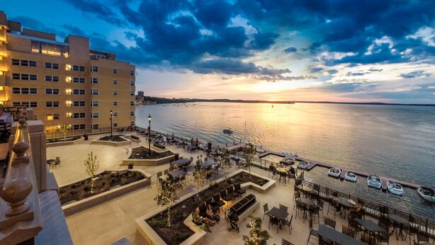 A waterfront hotel with outdoor seating and a view of the sunset over the water.