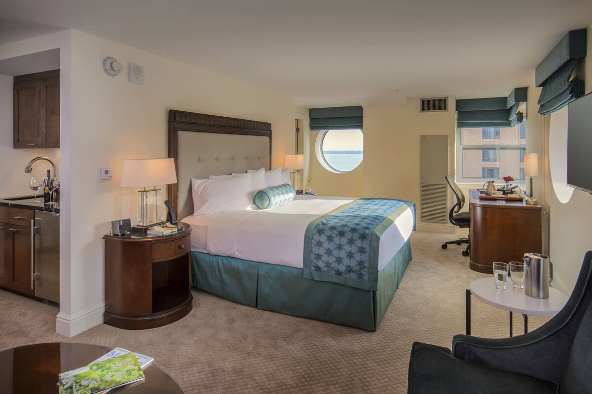 A hotel room with a bed, a desk, a chair, a small table, a window, and a view of the sea.