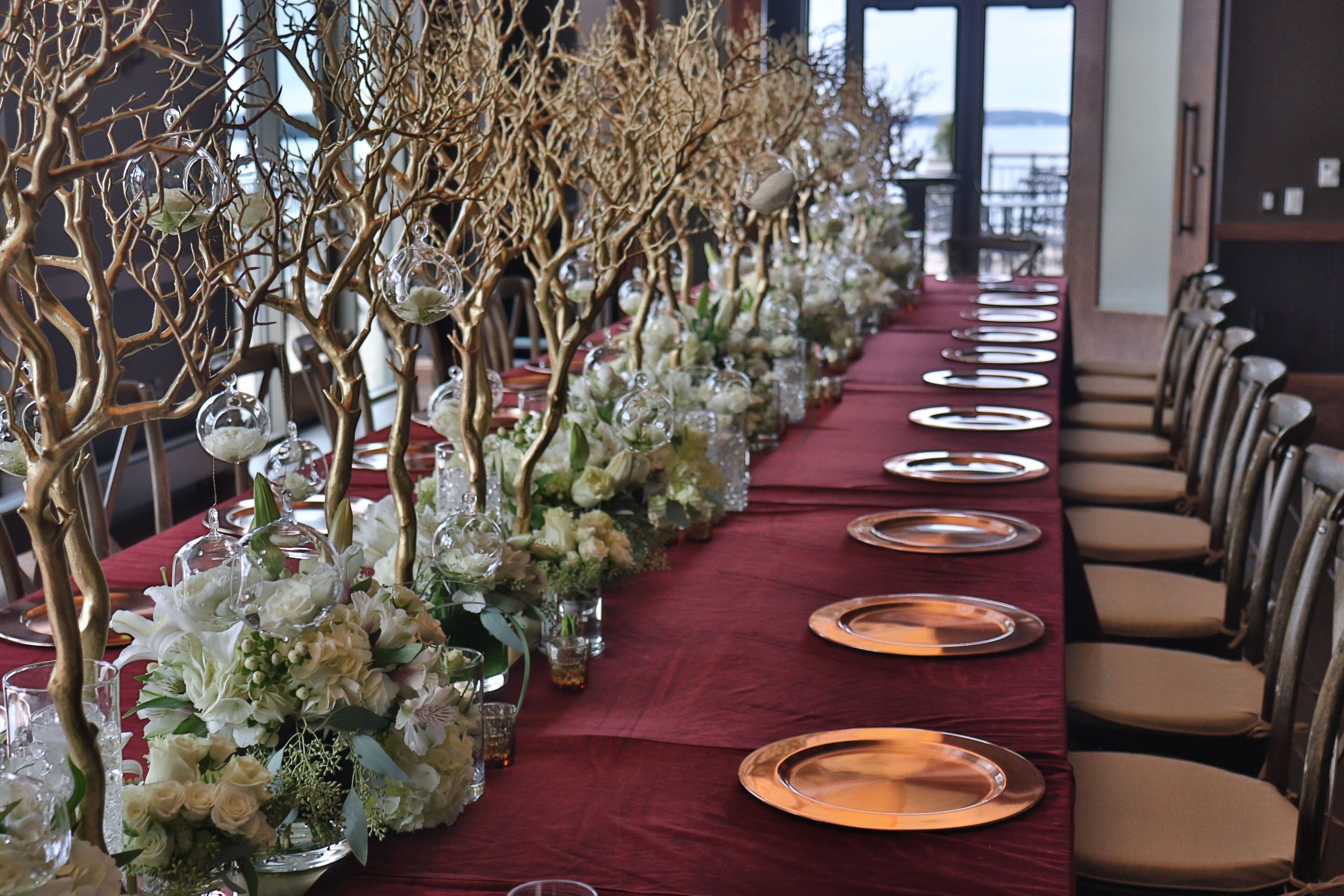 A long table set for a formal event with a red tablecloth, gold plates, and floral centerpieces.