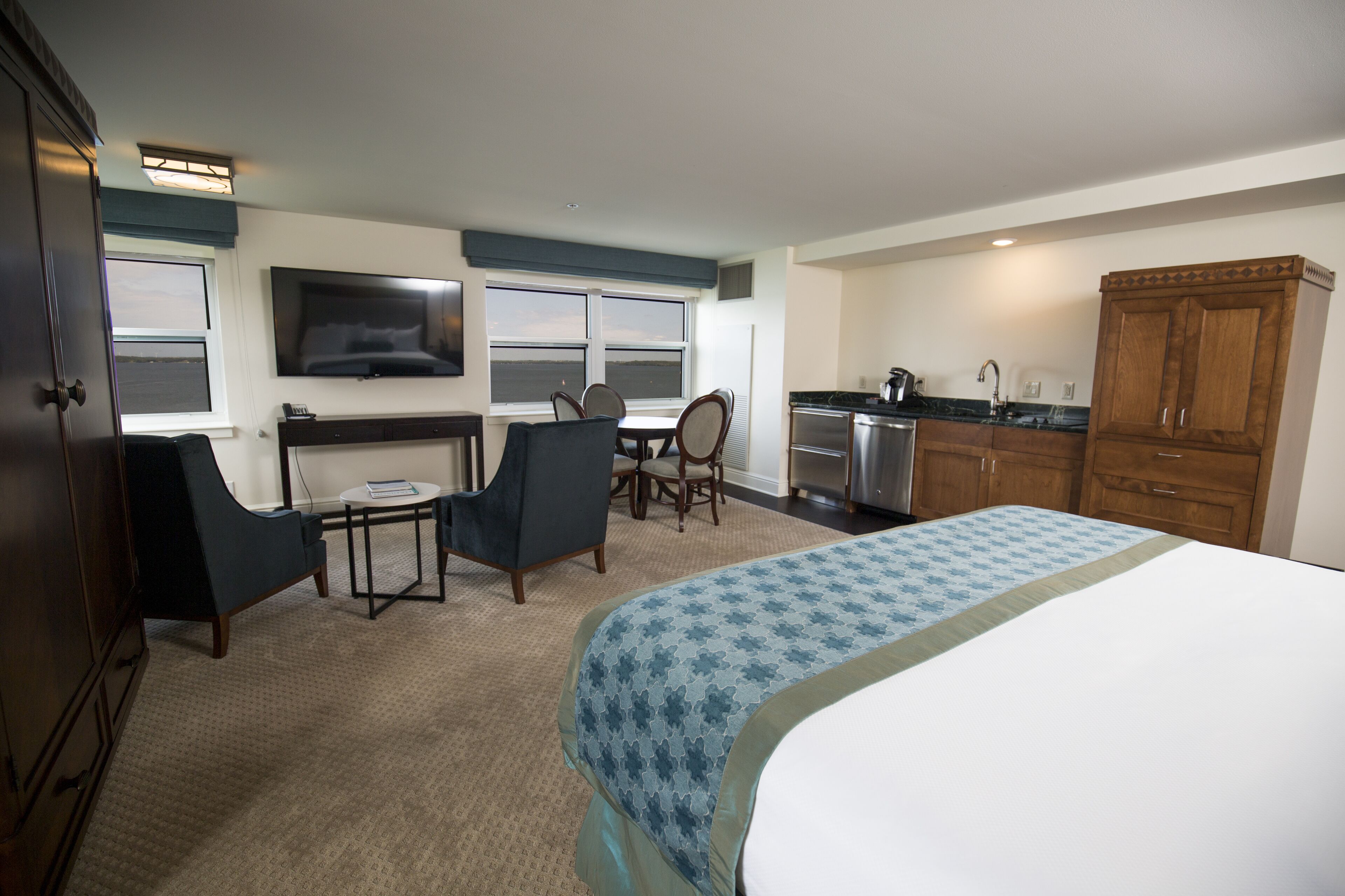 A hotel room with a bed, a desk, a chair, a television, and a kitchenette.