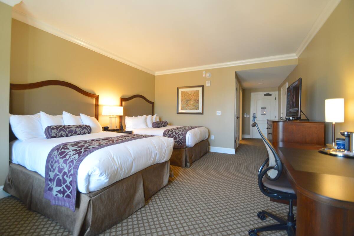 A hotel room with two beds, a desk, and a chair.