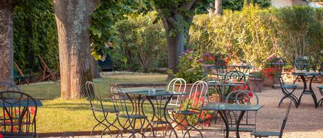 Un patio al aire libre con mesas y sillas, rodeado de árboles y plantas.
