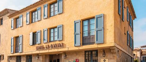 A two-story building with a stone facade and blue shutters. The sign reads "HOTEL LE DONJON".