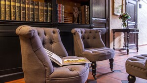 A library with bookshelves, two upholstered chairs, and a small table with a vase.