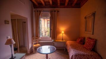 Ein Schlafzimmer mit einem Bett, einem Tisch, einem Stuhl, einer Lampe und einem Fenster mit Vorhängen.