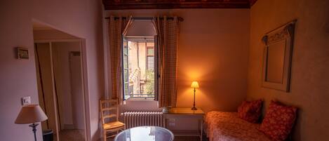 Un dormitorio con una cama, una mesa, una silla, una lámpara y un ventanal con cortinas.