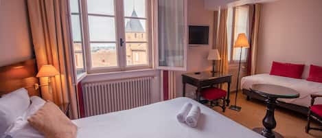 Habitación de hotel con dos camas, un escritorio, una silla, un televisor y vista a un edificio desde la ventana.