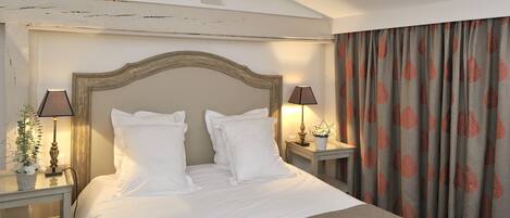 A neatly made bed with white linens and a wooden headboard, two bedside tables with lamps, and a curtain with a leaf pattern.