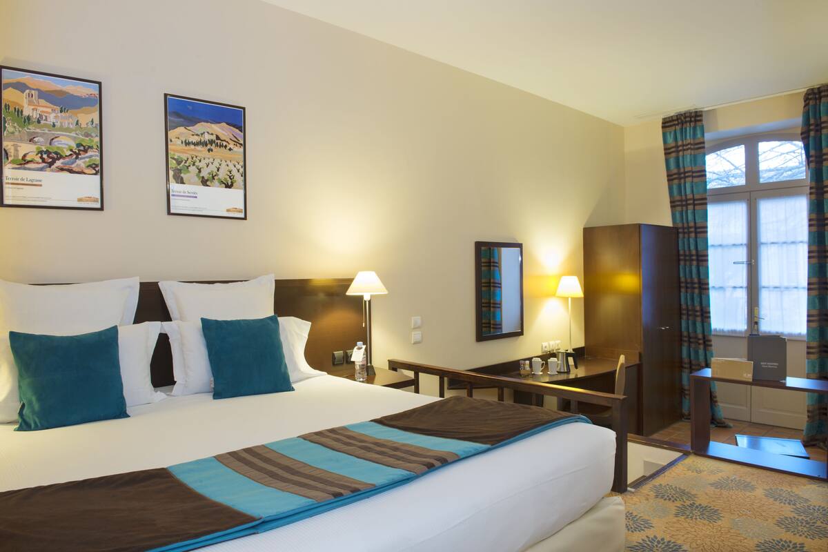 Ein Hotelzimmer mit einem großen Bett, zwei Nachttischen, einem Schreibtisch, einem Stuhl und zwei Lampen.