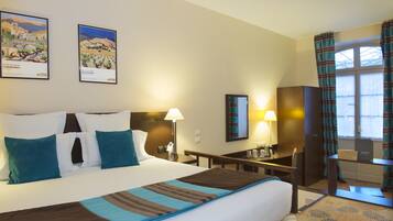 A hotel room with a large bed, two bedside tables, a desk, a chair, and two lamps.