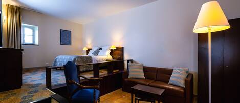 A hotel room with a bed, a sofa, a chair, a desk, and a lamp.
